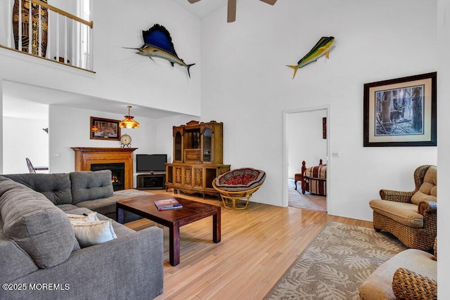 living room featuring ceiling fan, light hardwood / wood-style floors, and a towering ceiling