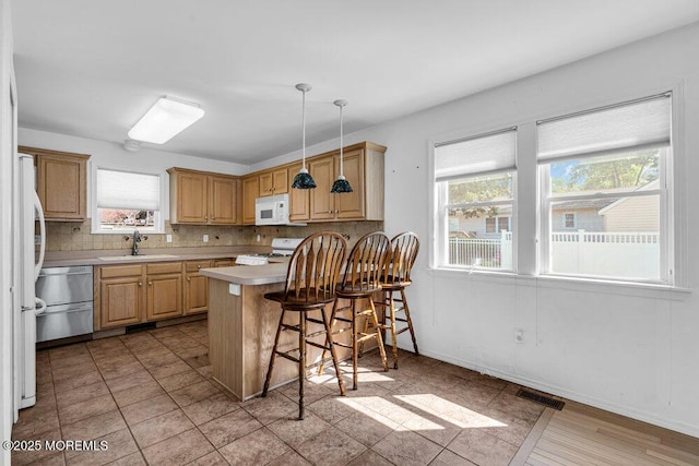 kitchen with a kitchen bar, decorative light fixtures, white appliances, light brown cabinetry, and sink