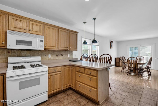 kitchen with hanging light fixtures, a healthy amount of sunlight, kitchen peninsula, and white appliances