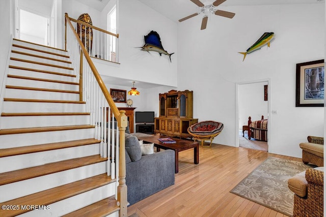 living room featuring ceiling fan, light wood-type flooring, and a high ceiling