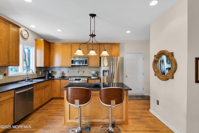 kitchen with light hardwood / wood-style floors, stainless steel appliances, decorative light fixtures, a kitchen island, and sink