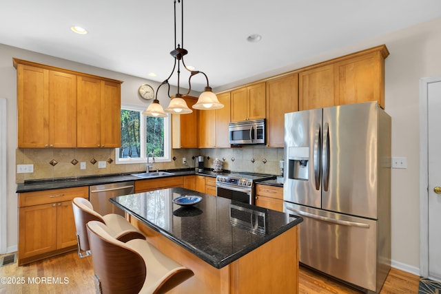 kitchen featuring appliances with stainless steel finishes, a center island, dark stone counters, sink, and hanging light fixtures