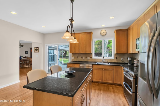 kitchen with light hardwood / wood-style floors, stainless steel appliances, a center island, decorative light fixtures, and sink