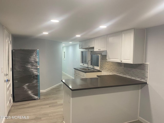 kitchen with tasteful backsplash, sink, white cabinets, kitchen peninsula, and light wood-type flooring