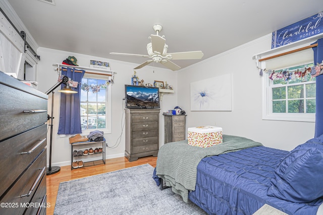 bedroom featuring ceiling fan, a barn door, ornamental molding, and hardwood / wood-style floors