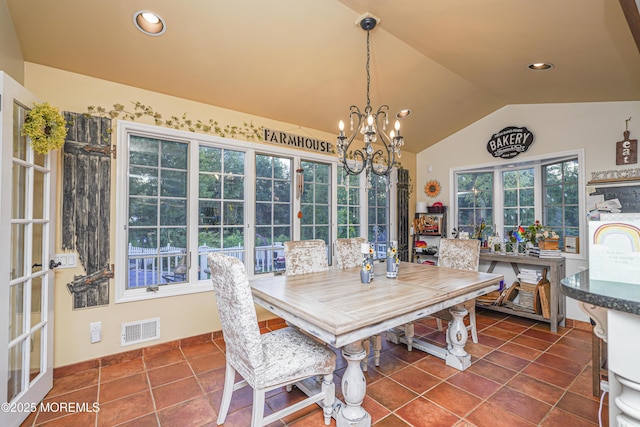 dining area with lofted ceiling, a healthy amount of sunlight, dark tile patterned flooring, and an inviting chandelier