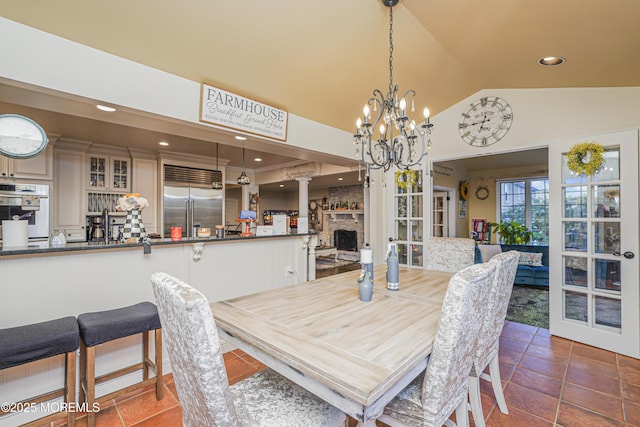 dining room with an inviting chandelier, dark tile patterned floors, lofted ceiling, and a fireplace