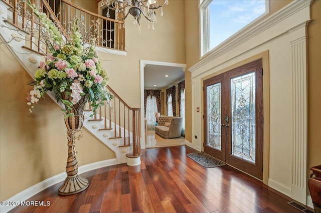 foyer entrance with french doors, a towering ceiling, an inviting chandelier, and hardwood / wood-style flooring