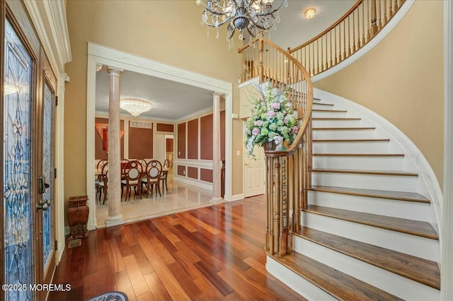 stairs with a notable chandelier, hardwood / wood-style flooring, crown molding, and ornate columns