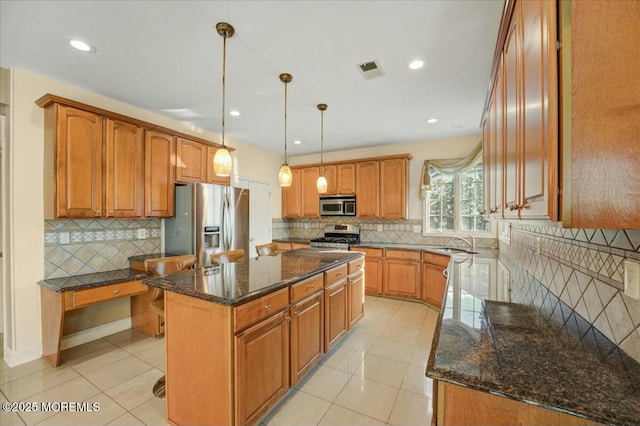 kitchen with pendant lighting, a kitchen island, stainless steel appliances, light tile patterned floors, and dark stone counters