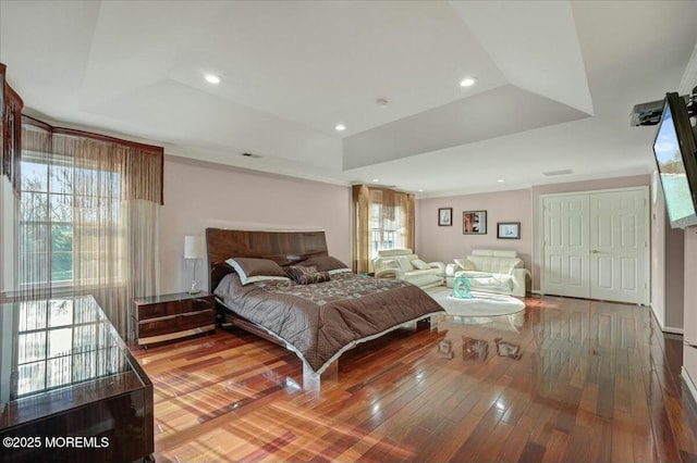 bedroom featuring hardwood / wood-style flooring, a closet, a raised ceiling, and multiple windows