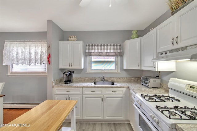 kitchen featuring a healthy amount of sunlight, baseboard heating, white cabinets, white gas range oven, and sink