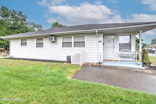 single story home with an AC wall unit, a porch, and a front yard