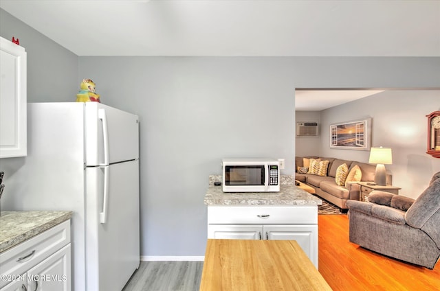 kitchen with light wood-type flooring, white appliances, white cabinetry, and a wall unit AC