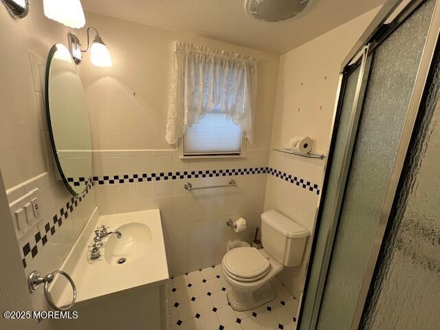 bathroom with toilet, vanity, tile walls, and an enclosed shower