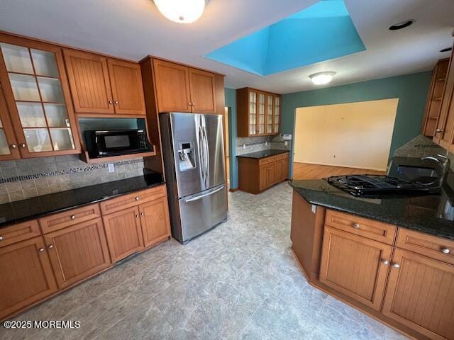 kitchen with stainless steel refrigerator with ice dispenser, dark stone countertops, decorative backsplash, sink, and a tray ceiling