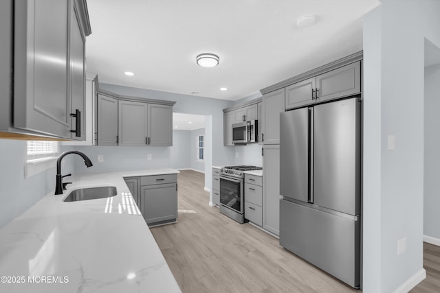 kitchen featuring sink, appliances with stainless steel finishes, gray cabinetry, light stone countertops, and light wood-type flooring