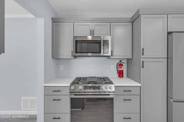 kitchen featuring crown molding, stainless steel appliances, light stone countertops, and gray cabinetry