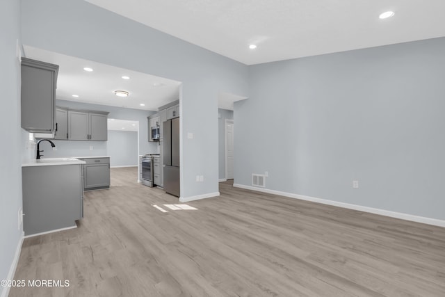 kitchen featuring stainless steel appliances, gray cabinets, sink, and light wood-type flooring