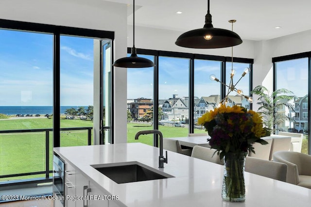 kitchen with decorative light fixtures, a water view, white cabinets, and sink