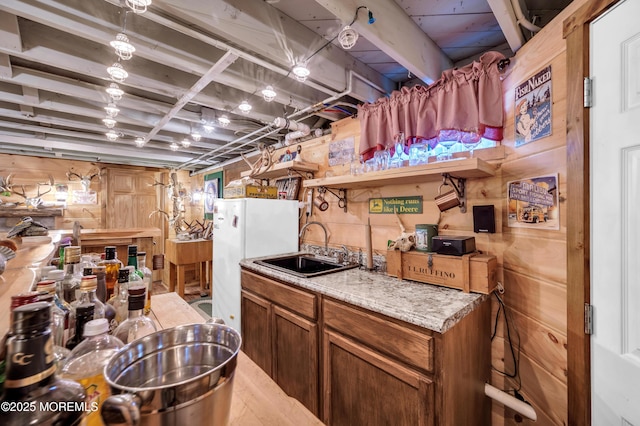 kitchen with light hardwood / wood-style floors, sink, white fridge, and wooden walls