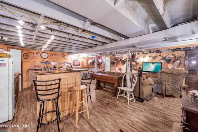 interior space with hardwood / wood-style flooring, indoor bar, white fridge, and wooden walls