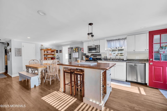 kitchen with a kitchen island, butcher block countertops, white cabinetry, hanging light fixtures, and appliances with stainless steel finishes