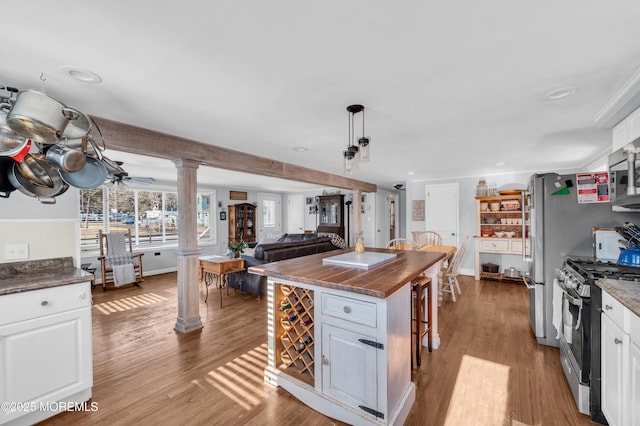 kitchen with decorative columns, white cabinets, stainless steel range with gas stovetop, and a center island