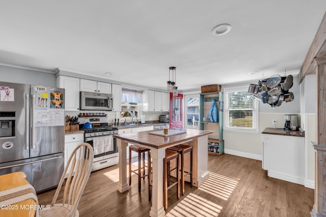 kitchen featuring white cabinetry, stainless steel appliances, decorative light fixtures, wood-type flooring, and a breakfast bar