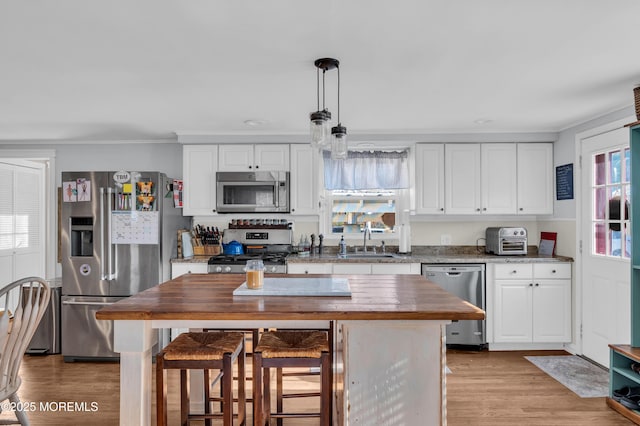 kitchen with appliances with stainless steel finishes, a healthy amount of sunlight, decorative light fixtures, white cabinets, and sink