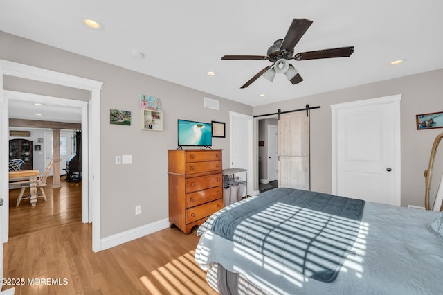 bedroom with ceiling fan, light hardwood / wood-style floors, and a barn door