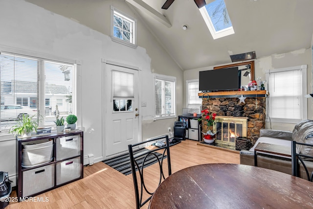 living room featuring a skylight, high vaulted ceiling, wood-type flooring, and a stone fireplace