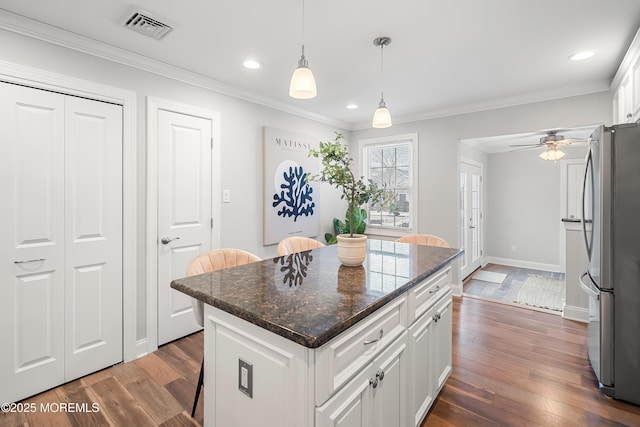 kitchen featuring dark wood-type flooring, a center island, a kitchen breakfast bar, stainless steel fridge, and white cabinets