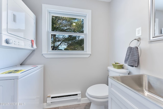 bathroom with vanity, stacked washer / drying machine, baseboard heating, and toilet