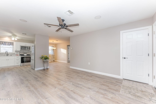 unfurnished living room with sink, ceiling fan with notable chandelier, and light wood-type flooring