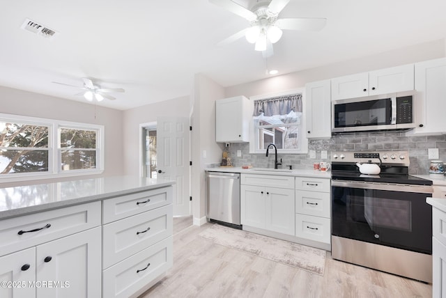 kitchen featuring appliances with stainless steel finishes, sink, backsplash, white cabinets, and light hardwood / wood-style floors