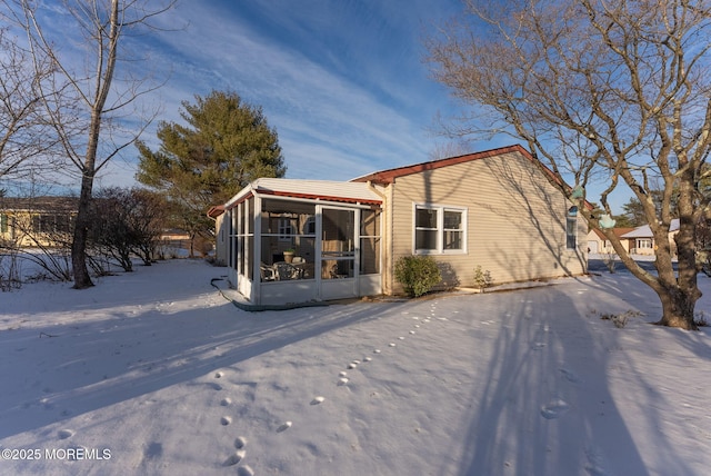 snow covered back of property featuring a sunroom