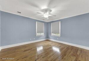 spare room featuring dark wood-style floors, ornamental molding, a ceiling fan, and baseboards