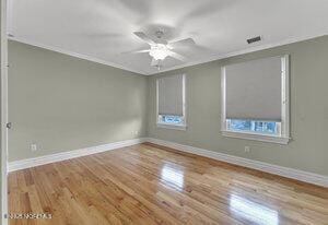 empty room featuring light wood-type flooring, visible vents, baseboards, and ornamental molding