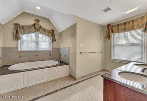 full bathroom with a sink, visible vents, vaulted ceiling, a bath, and double vanity