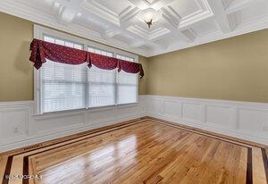 empty room with crown molding, wainscoting, wood finished floors, coffered ceiling, and beamed ceiling