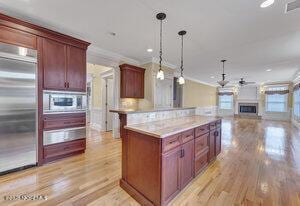 kitchen featuring reddish brown cabinets, decorative light fixtures, stainless steel appliances, light countertops, and open floor plan