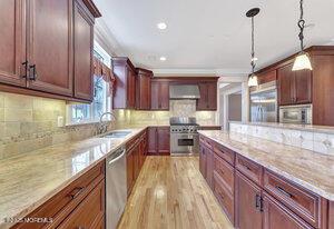 kitchen featuring light stone counters, hanging light fixtures, appliances with stainless steel finishes, a sink, and wall chimney range hood