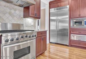 kitchen with light countertops, decorative backsplash, range hood, reddish brown cabinets, and high end appliances