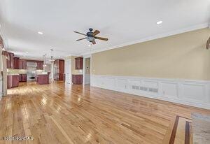 unfurnished living room featuring a wainscoted wall, a ceiling fan, ornamental molding, and wood finished floors