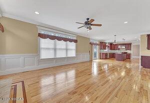 unfurnished living room with a decorative wall, light wood-style flooring, ornamental molding, a ceiling fan, and wainscoting