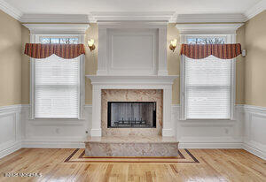 unfurnished living room with wainscoting, ornamental molding, a fireplace, and wood finished floors