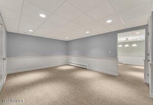 carpeted empty room with a baseboard heating unit, a drop ceiling, and recessed lighting