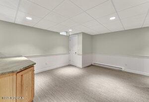 finished basement featuring a baseboard heating unit, carpet floors, a wainscoted wall, and a paneled ceiling