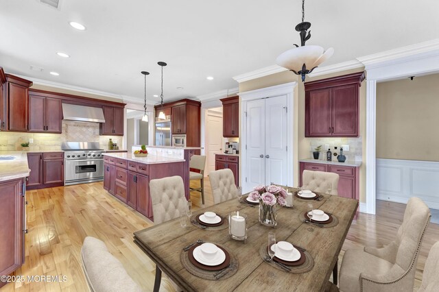 dining space featuring light wood finished floors, recessed lighting, crown molding, and a wainscoted wall